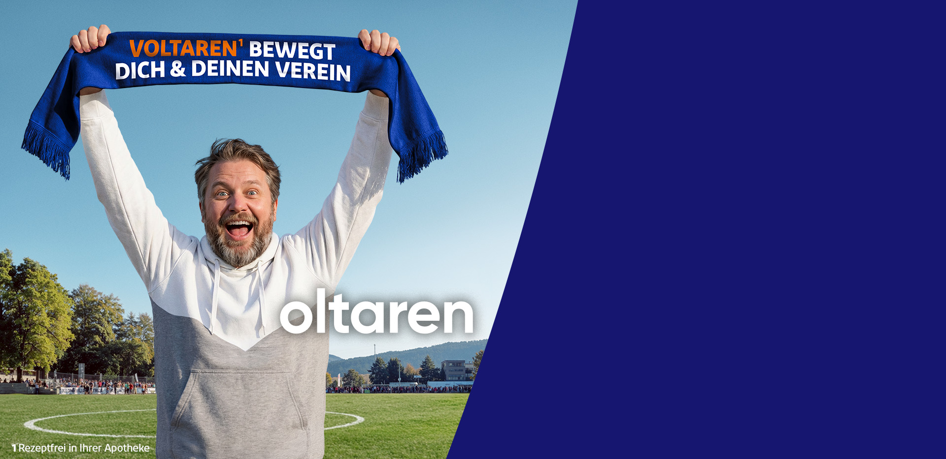 Person steht auf einem Fußballfeld und hält einen blauen Schal mit der Aufschrift 'Voltaren bewegt dich & deinen Verein' über den Kopf; im Hintergrund Spielfeld, Bäume und Zuschauer